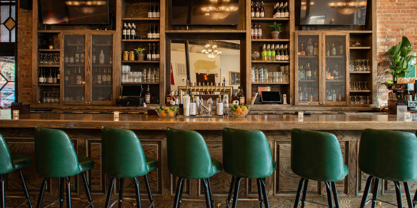 green cushioned bar stools lined up at the bar area of the Piggy Bank